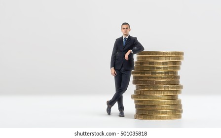 Full growth portrait of a businessman leaning on a stack of big golden coins on a white background. Earning a stable income. Feeling confident about your money. Providing revenue.