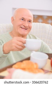 Full Of Happiness. Close Up Of Delighted Adult Man Sitting In The Arm Chair And Getting Cup From The Tray In  Hands Of His Loving Wife