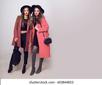 Full height   studio image of two fashionable sexy woman in casual trendy spring coat,  boots with heels , black hat, stylish hand bag. 
