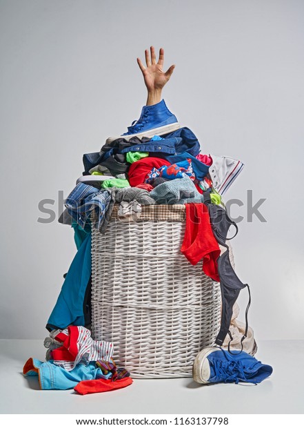 Full laundry white wicker basket, with a hand\
sticking out, on the grey\
background
