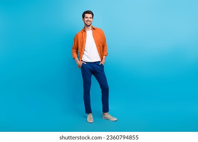 Full lenght photo of cheerful charming man dressed orange shirt smiling hands arms pockets isolated blue color background - Powered by Shutterstock