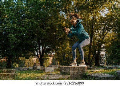 Full lenght portrait of beautiful fitness woman doing squat box jumps in the park. - Powered by Shutterstock