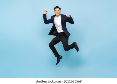 Full lenght portrait of ecstatic handsome Asian man jumping and raising  his fists on isolated light blue studio background