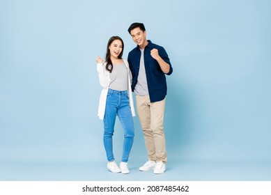 Full lenght portrait of young smiling Asian couple holding each other and clenching fists in isolated light blue studio background - Shutterstock ID 2087485462