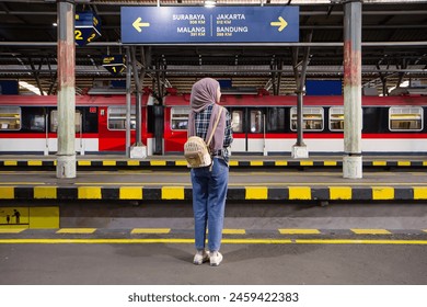 full lenght shoot of back view asian muslim woman standing on train platform with directions sign and train on the background. traveling concept - Powered by Shutterstock