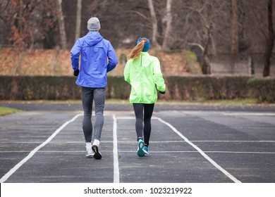 Full Lenght Shot From Behind Of A Young Couple Running Outdoors.