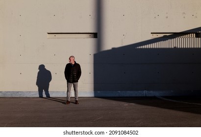 Full length of adult man in winter clothes standing against white wall with sunlight and shadow - Powered by Shutterstock