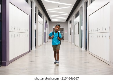 Full length of african american elementary schoolboy with backpack walking in school corridor. unaltered, education, childhood, boredom and school concept.