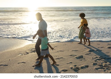 Full Length Of African American Family Walking On Shore At Beach During Sunset. Unaltered, Family, Lifestyle, Togetherness, Enjoyment And Holiday Concept.