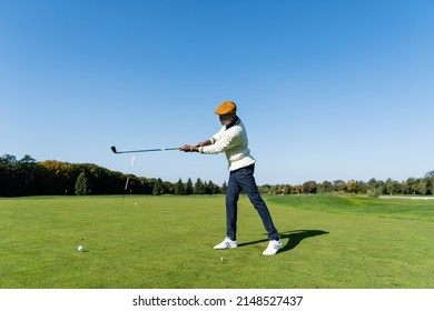 Full Length Of African American Man In Flat Cap Holding Golf Club And Playing On Green Lawn