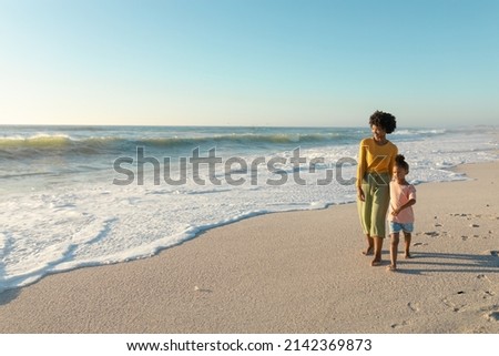 Full length of african american mother and daughter walking on shore at beach with copy space. unaltered, family, lifestyle, togetherness, enjoyment and holiday concept.