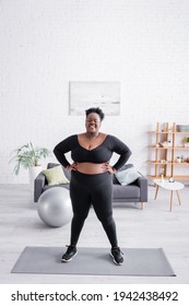 Full Length Of African American Plus Size Woman In Sportswear Standing With Hands On Hips On Fitness Mat