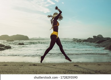 Full length of african woman in bikini running on the beach. Female model on the sea shore enjoying herself.