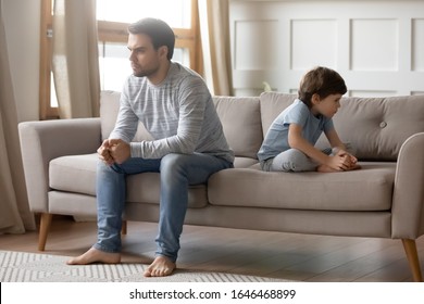 Full Length Annoyed Young Father Sitting Back To Back With Little Son On Sofa, Ignoring Each Other After Argue. Disappointed By Bad Kids Behavior Dad Not Talking To Child, Family Problems Concept.