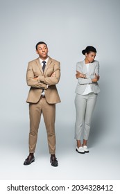 Full Length Of Arrogant Businessman With Crossed Arms Near Upset African American Woman On Grey