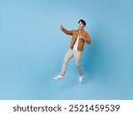 Full length Asian man jumping with hand pointing finger isolated on blue copy space background. 