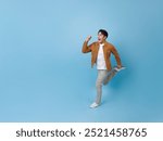 Full length Asian man running hurry up with excited smile isolated on blue background. Happy man joyful run in copy space.