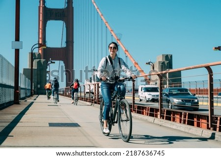 full length asian woman is enjoying cityscape while cycling at leisure on golden gate bridge in San Francisco California on a sunny day with vehicles passing by