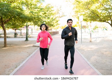 Full Length Of An Athletic Couple Running Together In The Park. Beautiful Latin Woman And Handsome Latin Man Jogging In The Running Track