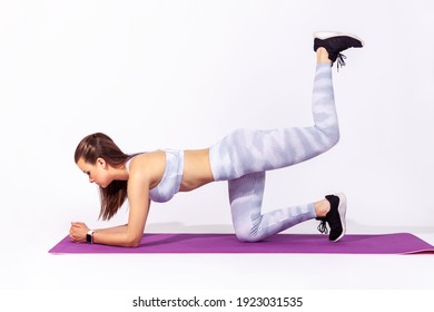 Full Length Athletic Woman In White Sportswear Practicing Yoga, Doing One Legged Plank Pose Bow Leg, Training Muscle Flexibility. Indoor Studio Shot Isolated On Gray Background