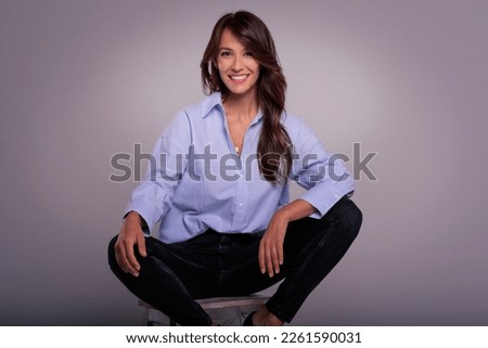 Full length of attractive middle aged woman cheerful smiling and wearing blue shirt against dark background. Copy space. Studio shot.