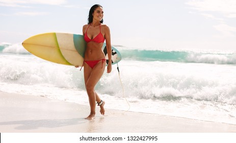 Full length of attractive woman coming out of the sea with surfboard. Smiling woman walking out of sea water after surfing. - Powered by Shutterstock