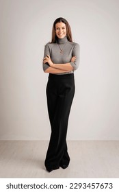Full length of an attractive woman toothy smiling and looking at camera. Brunette haired female wearing turtleneck sweater and trousers while standing against isolated white background. Copy space.  - Shutterstock ID 2293457673