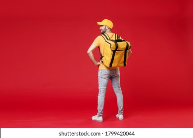 Full length back rear view of delivery employee man 20s in yellow cap t-shirt uniform thermal food bag backpack work courier service in quarantine covid-19 standing isolated on red background studio