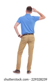 Full Length Back View Picture Of A Young Casual Man Thinking While Holding A Hand On His Waist And Scratching His Head With The Other. Isolated On A White Background