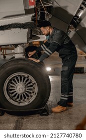 Full Length Of Bearded Man Aviation Maintenance Technician Repairing Aircraft Landing Gear At Repair Station