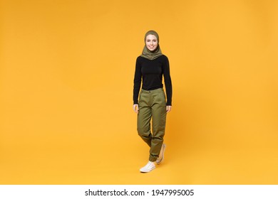 Full Length Of Beautiful Young Arabian Muslim Woman In Hijab Black Green Clothes Standing Looking Camera Isolated On Bright Yellow Color Background Studio Portrait. People Religious Lifestyle Concept