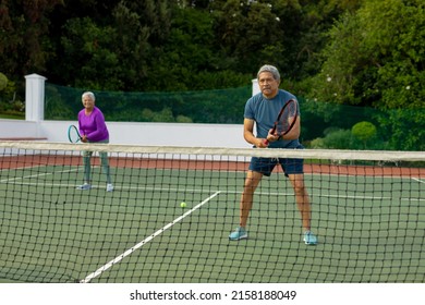 Full length of biracial senior man playing tennis with senior woman in tennis court against trees. unaltered, sport, competition, togetherness, love, retirement, healthy and active lifestyle. - Powered by Shutterstock