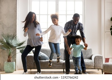 Full Length Black African Whole Family Have A Fun. Married Couple With Little Kids Toddler Son Preschool Daughter Dancing Moving In Living Room At New Home. Happy Family Spend Time Together Concept