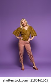 Full Length Of Blonde Woman With Menopause Posing With Hands On Hips And Smiling On Purple