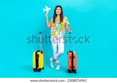 Full length body cadre of optimistic cute korean girl hold paper airplane lowcost transport luggage isolated on aquamarine color background