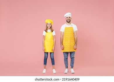 Full Length Body Of Confident Teen Girl Dad Man Father's Helper Chef Cook Confectioner Baker Wearing Yellow Apron Toque Cap Standing Looking Camera Isolated On Pastel Pink Background Studio Portrait