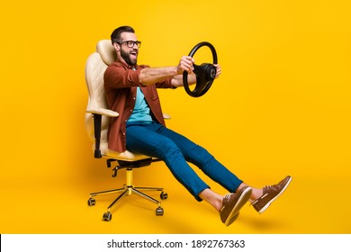 Full length body photo of playful crazy man in chair holding steering wheel pretending car rider isolated vivid yellow color background