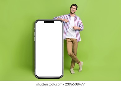 Full length body photo of young handsome businessman promoter marketing directing finger phone display isolated on green color background