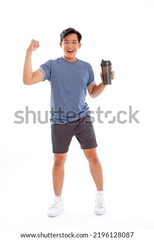 Full length body photo of a young Asian man with muscular body holding a shake bottle tumbler and drink with one hand stand facing on isolated background.