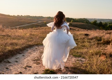 Full length body portrait of beautiful bride in white wedding dress running in the field on sunset, back view. Wedding concept - Powered by Shutterstock