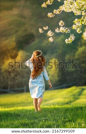 Full length body portrait of beautiful woman in blue dress with long hair running away through green hills during spring. 
