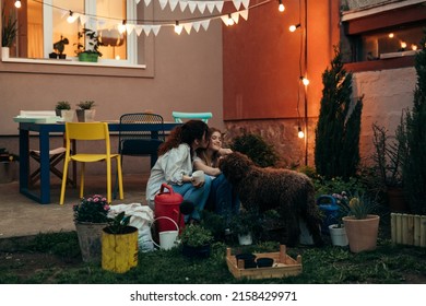 Full Length Body Shoot Of Mother And Daughter Gardening In Backyard. They Are Hugging