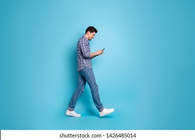 Full length body size photo of slender positive handsome carefree glad optimistic guy holding using telephone in hands going somewhere isolated pastel background
