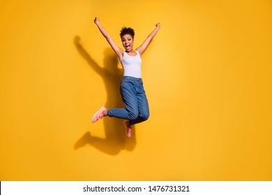 Full length body size photo funny nice beautiful she her dark skin model lady jumping high champion overjoyed yelling loud wear casual jeans denim pants trousers tank-top isolated yellow background