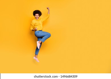 Full length body size photo of jumping curly wavy strong and powerful black woman rejoicing with her victorious glory fame wearing jeans denim pullover isolated bright color background
