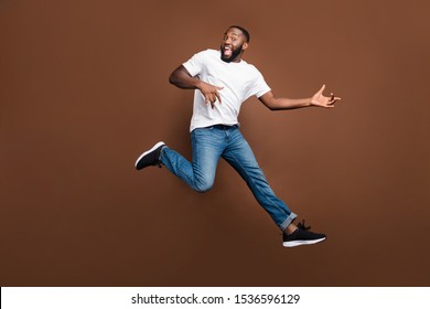 Full Length Body Size Photo Of Trendy Stylish Cheerful Handsome Guy Running Jumping Playing Guitar In Air Wearing White T-shirt Casual Jeans Denim Footwear Isolated Over Pastel Brown Color Background