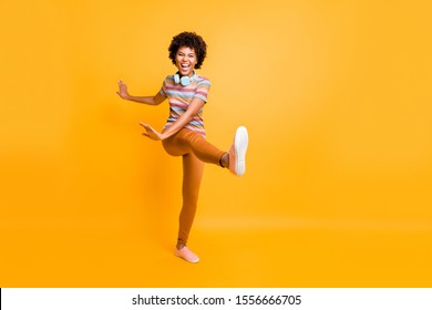 Full length body size photo of cheerful cute nice girlfriend throwing her leg ahead dancing grimacing behaving like a child wearing striped t-shirt pants trousers isolated over vivid color background