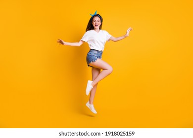 Full length body size photo of cheerful girl jumping high wearing jeans shorts white t-shirt headband on bright yellow color background