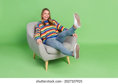 Full length body size photo laughing girl sitting in grey chair isolated pastel green color background