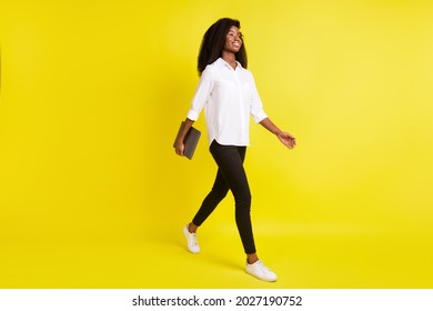 Full length body size photo smiling girl walking forward keeping laptop looking blank space isolated bright yellow color background